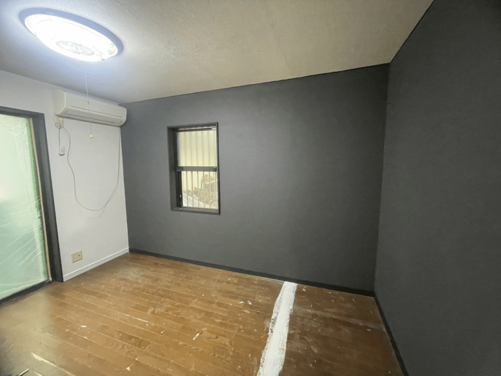 江東区のマンションでクロス張り作業中。明るいグレーのクロスを貼り、丁寧に空気を抜きながら仕上げている様子。