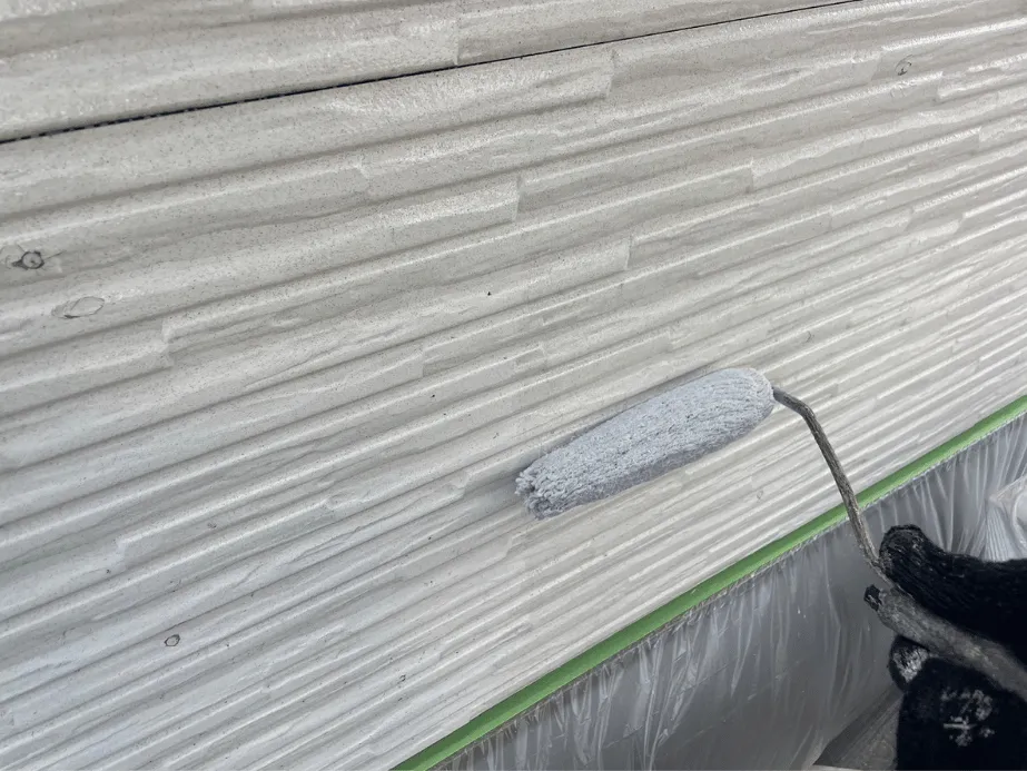 【施工レポート】外壁の下塗り|塗装の耐久性を決める最重要工程 5 凹凸のある白系サイディング外壁へ下塗り材をローラーで丁寧に塗り込んでいる様子