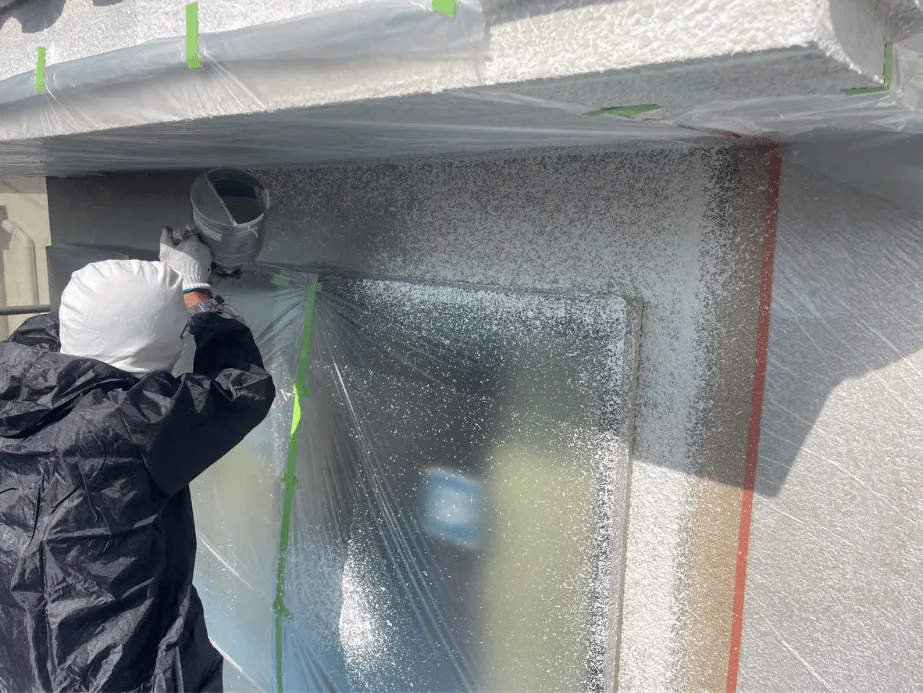 職人がスプレーガンで外壁上部を吹付塗装する様子｜丁寧な塗布でムラのない仕上がりに
